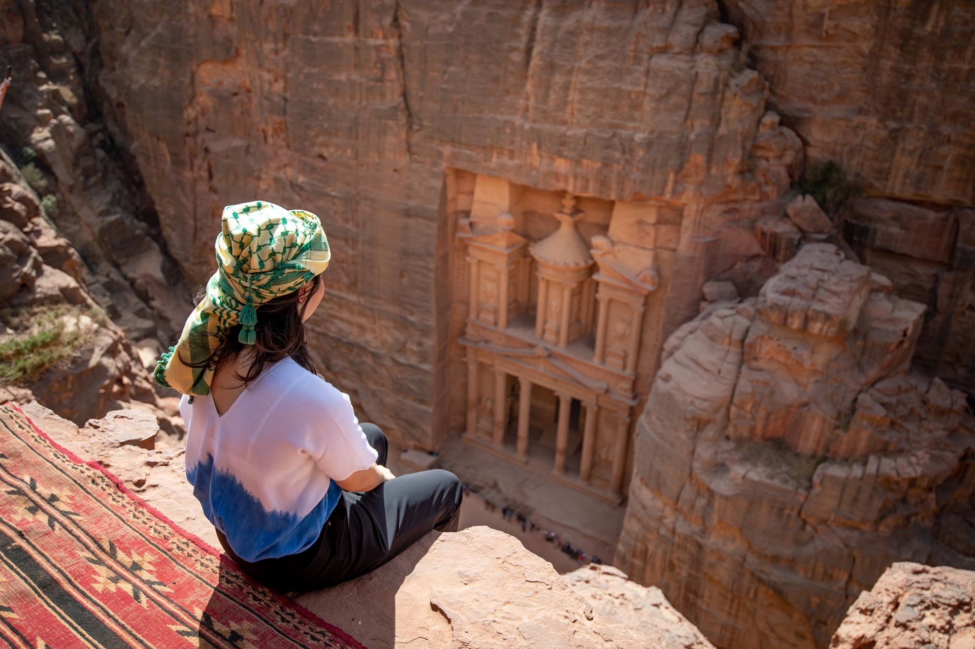 A woman traveler sitting on carpet viewpoint in Petra ancient city looking at the Treasury or Al-khazneh, famous travel destination of Jordan and one of seven wonders. UNESCO World Heritage site. A woman traveler sitting on carpet viewpoint in Petra ancient city looking at the Treasury or Al-khazneh, famous travel destination of Jordan and one of seven wonders. UNESCO World Heritage site.